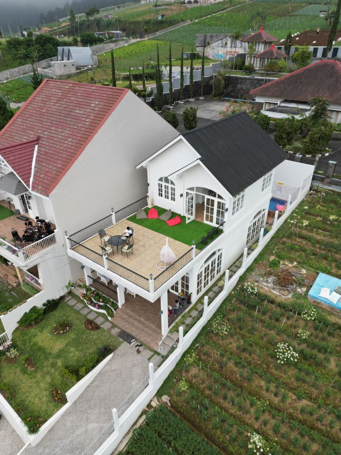 Aerial shot of modern white house with lush garden and terrace seating.